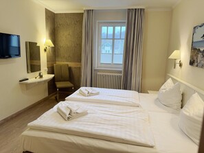 A hotel room with two beds, a television, a chair, a window with curtains, and a painting on the wall.