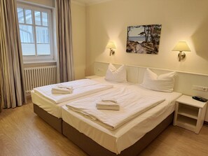 Quarto de hotel com cama de casal, duas mesas de cabeceira, janela com cortinas, luminária na parede e um quadro.