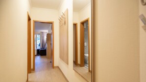 Een gang met houten vloeren en lichte wanden, die leidt naar een kamer met een bed en een raam.