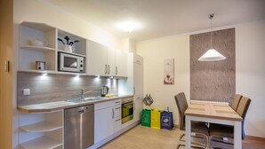 Een moderne keuken met witte kasten, een ingebouwde magnetron en een eethoek met een houten tafel en stoelen.