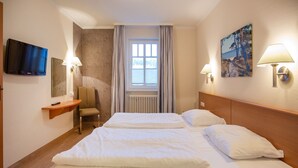 Een hotelkamer met twee bedden, een televisie, een stoel, een bureau en een raam met gordijnen.