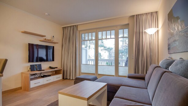 Een moderne woonkamer met een grote bank, een salontafel, een televisie en een balkon met gordijnen.