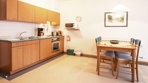 A compact kitchen with wooden cabinets, a microwave, and a dining area with a table and chairs. - Classic apartment with 1 bedroom and balcony on the top floor (Ostseebad Binz)