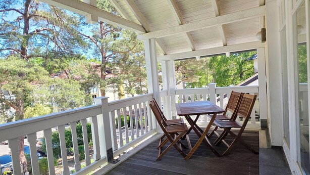 A covered porch with a white railing, a table, and two chairs. - Classic apartment with 1 bedroom and balcony on the top floor (Ostseebad Binz)