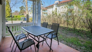 Eine überdachte Terrasse mit Tisch und Stühlen, mit Blick auf eine Wohngegend mit Häusern und Bäumen.