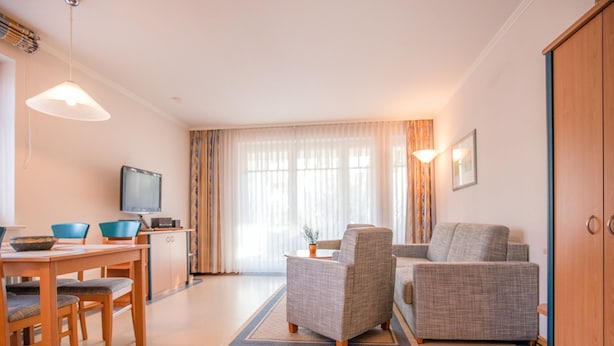 Ein modernes Wohnzimmer mit Essbereich, Fernseher und einem großen Fenster mit Vorhängen.