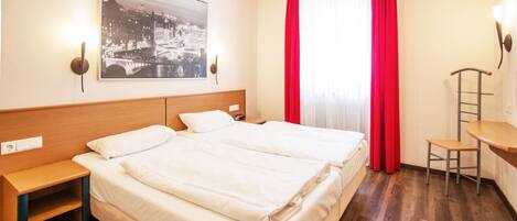 Une chambre d’hôtel avec deux lits, un bureau, une chaise et une grande fenêtre avec des rideaux rouges.