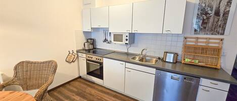 A compact kitchen with white cabinets, a microwave, a stove, and a sink.