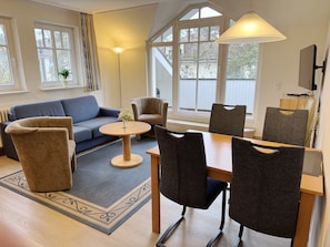 A modern living room with a sofa, armchairs, a dining table, and a TV.