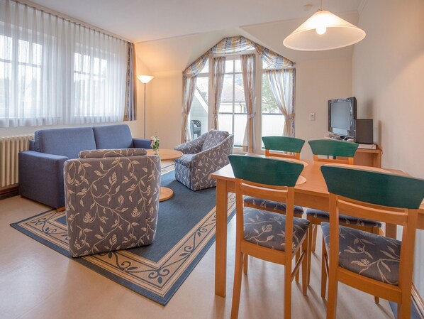 A modern living room with a sofa, chairs, a dining table, and a TV. - Comfort apartment with 2 bedrooms and balcony on the top floor (Ostseebad Binz)