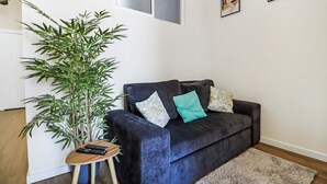 Een woonkamer met een donkerblauwe bank, een klein houten bijzettafeltje, een grote groene plant en een zacht vloerkleed.