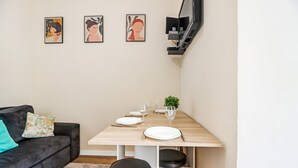 Een moderne woonkamer met een bank, een eettafel gedekt voor twee personen en drie ingekaderde kunstwerken aan de muur.
