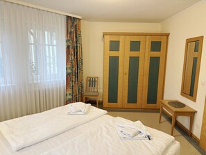 Habitación de hotel con dos camas, una silla, una mesita y un armario.