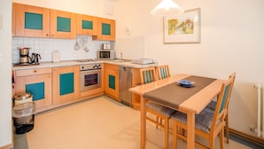 Une cuisine compacte avec des meubles en bois, un four à micro-ondes, une cuisinière et un évier. On y trouve une table à manger avec des chaises et un saladier bleu posé dessus.