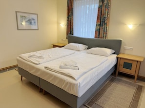 A neatly made bed with white linens and towels, a grey upholstered headboard, and a small bedside table with a lamp. - Comfortable 2-Bedroom Apartment with a Terrace on the First Floor (Ostseebad Binz)