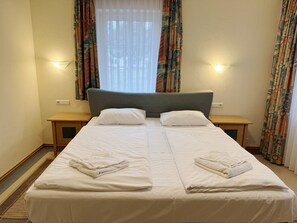A double bed with white linens, two bedside tables, and curtains with a pattern. - Comfort apartment with 2 bedrooms and terrace on the first floor (Ostseebad Binz)