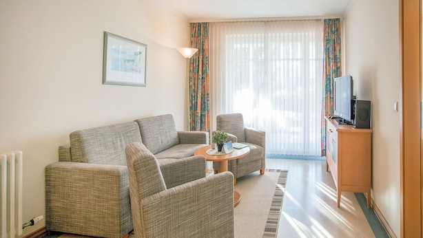 Un salon comprenant un canapé, deux fauteuils, une table basse, un téléviseur et un radiateur.