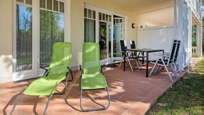 Une terrasse avec une table et des chaises, une porte-fenêtre coulissante et un espace abrité délimité par une clôture blanche.