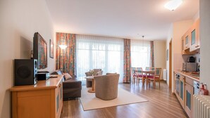 Un salon moderne comprenant un canapé, un fauteuil et une table à manger. Il y a également un coin cuisine avec des placards et des appareils électroménagers.
