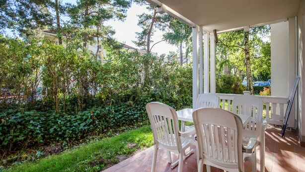 Une terrasse couverte avec une table et des chaises, entourée de verdure et offrant une vue sur la rue.