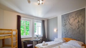 A room with bunk beds, a desk, and a chair. There are windows with curtains, a wall with a textured design, and a ceiling light fixture. - Comfort plus apartment with 2 bedrooms and balcony on the upper floor (Ostseebad Binz)