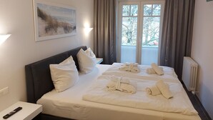 Quarto de hotel com cama grande, mesa de cabeceira, controle remoto, um quadro e janela com cortinas.
