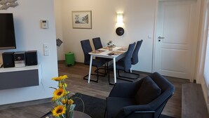 Uma sala de estar moderna com área de jantar, televisão de tela plana, relógio e uma porta.