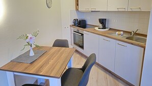 A compact kitchen with white cabinets, a wooden countertop, a coffee maker, and a clock on the wall. - Komfortplus Ferienwohnung mit 1 Schlafzimmer und Balkon im Dachgeschoss (Ostseebad Binz)