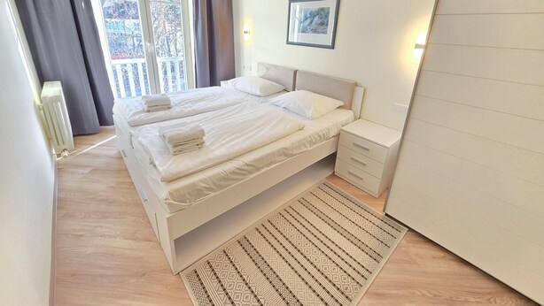 A hotel room with two beds, a large window with curtains, a framed picture on the wall, and a wooden floor. - Komfortplus Ferienwohnung mit 1 Schlafzimmer und Balkon im Dachgeschoss (Ostseebad Binz)