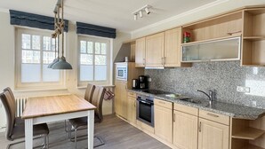 A modern kitchen with wooden cabinets, a granite countertop, a built-in oven, and a dining area with a table and chairs. - Comfort apartment with 1 bedroom and terrace on the first floor (Ostseebad Binz)