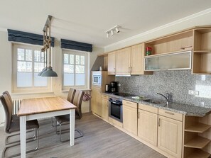 A modern kitchen with wooden cabinets, a granite countertop, a built-in oven, and a dining area with a table and chairs. - Comfort apartment with 1 bedroom and terrace on the first floor (Ostseebad Binz)