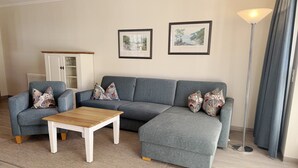A living room with a grey sectional sofa, a wooden coffee table, a cabinet with glass doors, and two framed pictures on the wall. - Comfort apartment with 1 bedroom and terrace on the first floor (Ostseebad Binz)
