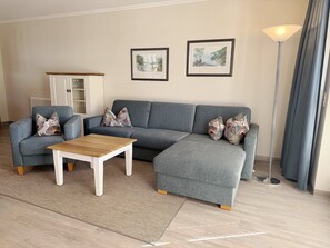 A living room with a grey sectional sofa, a wooden coffee table, a cabinet with glass doors, and two framed pictures on the wall. - Comfort apartment with 1 bedroom and terrace on the first floor (Ostseebad Binz)