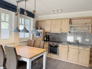 A modern kitchen with wooden cabinets, a granite countertop, a dining table with chairs, and pendant lights. - Comfortable 1-Bedroom Apartment with a Terrace on the First Floor (Ostseebad Binz)
