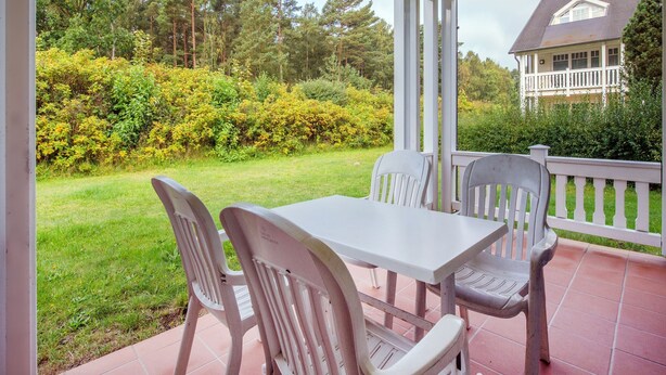 A covered patio with a table and chairs, surrounded by a garden and a house in the background. - Comfort apartment with 1 bedroom and terrace on the first floor (Ostseebad Binz)