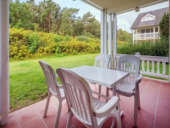 A covered patio with a table and chairs, surrounded by a garden and a house in the background.