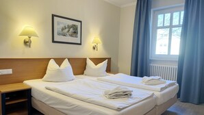 A hotel room with a double bed, two bedside lamps, a framed picture on the wall, and a window with curtains. - Comfort apartment with 1 bedroom and terrace on the first floor (Ostseebad Binz)