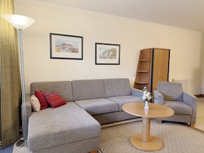 A living room with a grey sofa, a round coffee table, and two framed pictures on the wall. - Comfort apartment with 1 bedroom and terrace on the first floor (Ostseebad Binz)
