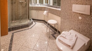 Et moderne badeværelse med en glasafskærmet bruseniche, et hvidt toilet og en gulvbelagt med marmor.