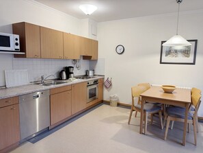 A modern kitchen with wooden cabinets, stainless steel appliances, a dining table with chairs, and a wall-mounted clock. - Comfort apartment with 1 bedroom and terrace on the first floor (Ostseebad Binz)