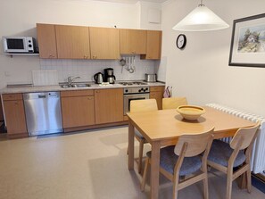 Une cuisine compacte avec des meubles en bois, un four à micro-ondes, un lave-vaisselle et une cuisinière. On y trouve une table à manger avec des chaises et un saladier posé dessus.