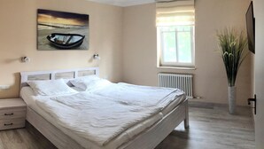 Un dormitorio con una cama grande, una mesita de noche, una ventana con persianas, un radiador y un cuadro de un barco en la pared.