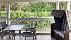 Un espacio al aire libre cubierto con mesa y sillas, un banco acolchado y vistas a un área boscosa.