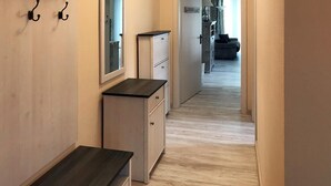 Un estrecho pasillo con suelo de madera, un banco oscuro y un armario blanco con cajones.