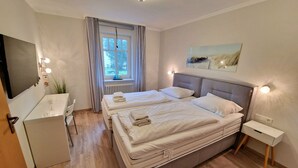 A modern bedroom with a double bed, bedside tables, a desk, and a TV.