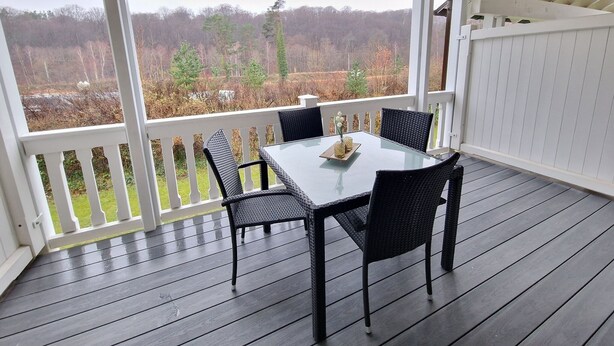 A covered patio with a table and chairs, overlooking a wooded area.