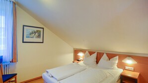 Una camera d'albergo con un letto, due comodini con lampade, una sedia, un termosifone e un quadro appeso al muro.
