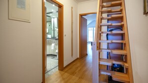 Ein Flur mit einer Holztreppe, einer zur Toilette führenden Tür und einem gerahmten Aushang an der Wand.