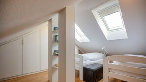 Ein kleines, modernes Schlafzimmer mit schrägverlaufender Decke, integriertem Kleiderschrank und Dachfenster.