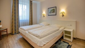 A double bed with two pillows, a bedside table, a chair, and a window with curtains. - Comfort apartment with 1 bedroom and terrace on the first floor (Ostseebad Binz)